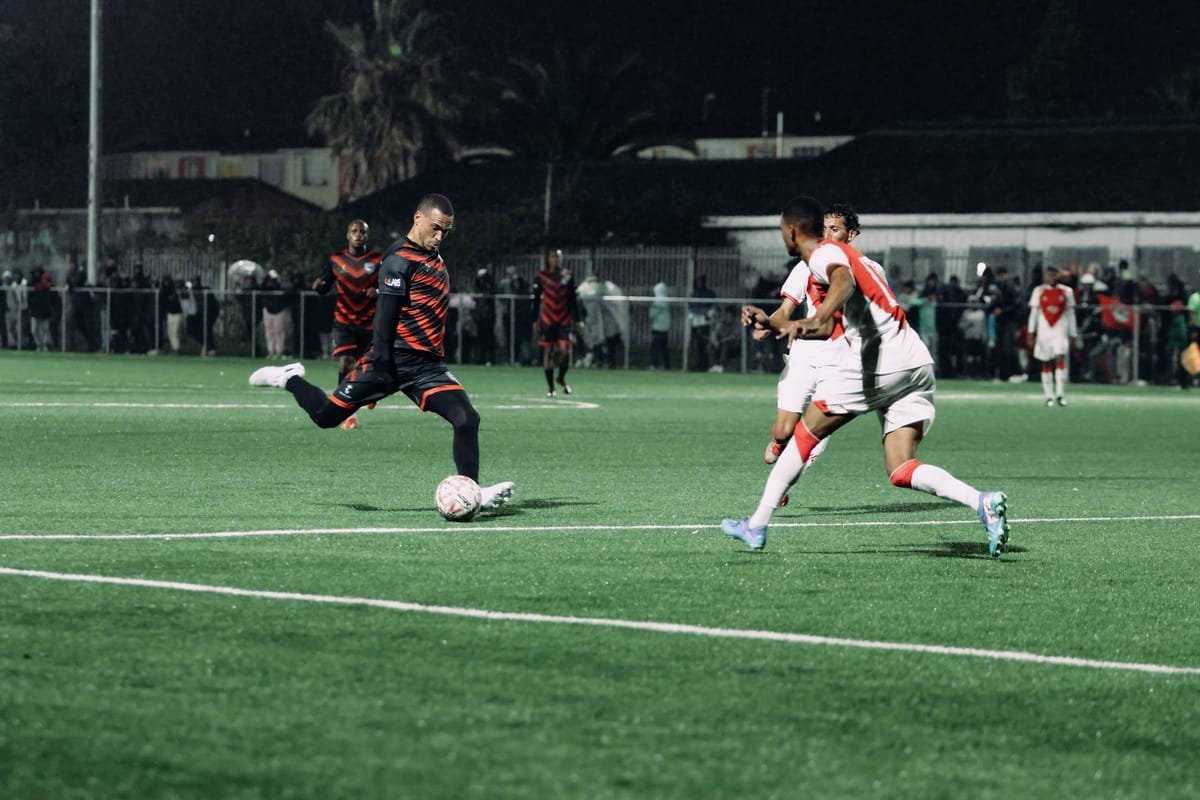 A Hope FC player striking the ball during a floodlit match