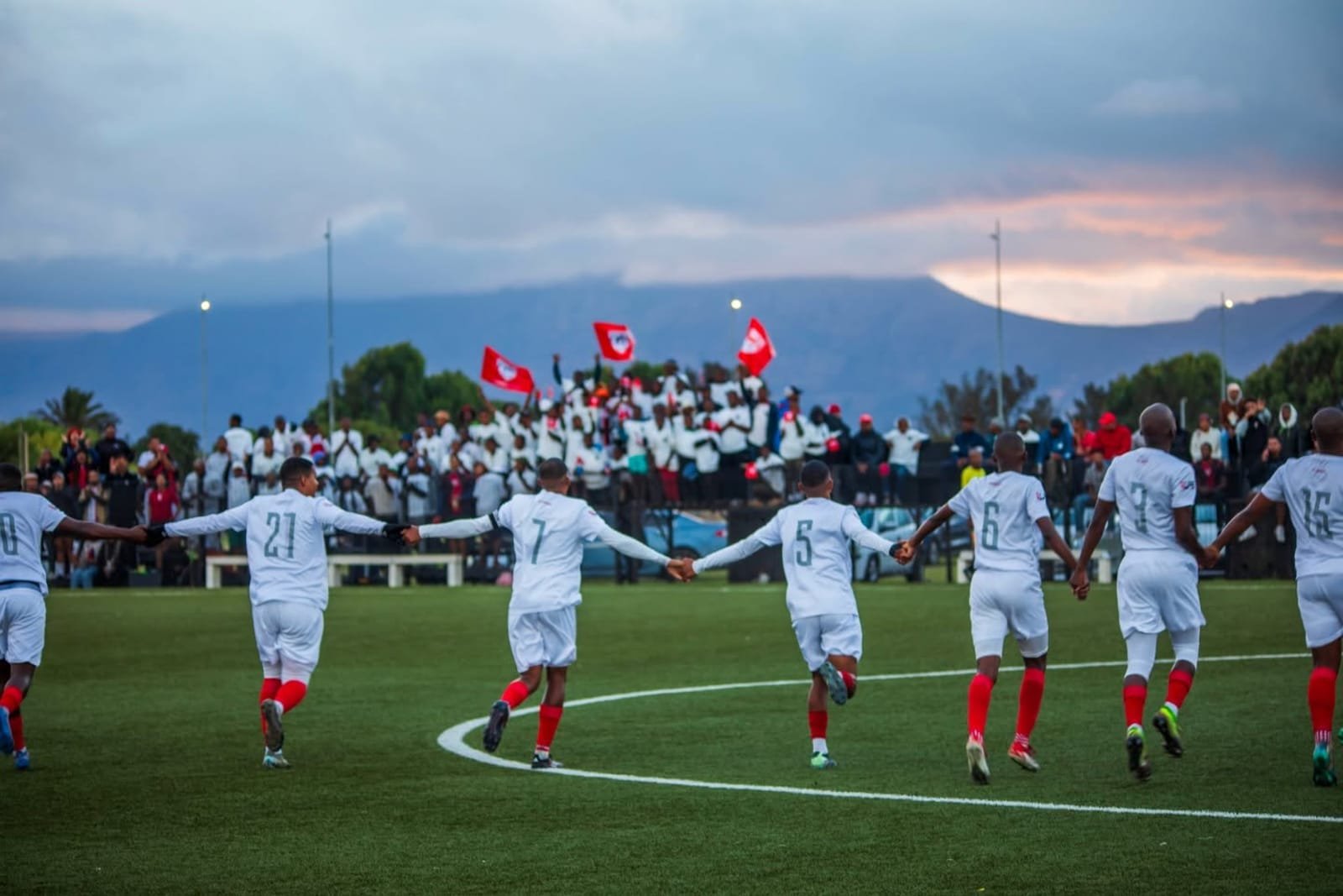 Hope FC players celebrate in front of fans waving red flags at Erica Park